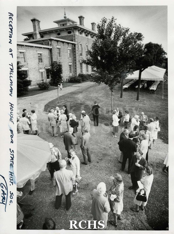 Black and white photograph of the reception at Tallman House for State Historical Society. Shows men and women standing in groups conversing.