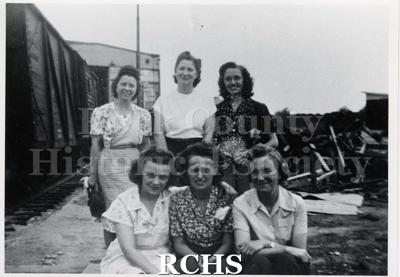 Black and white photograph of women from cushion line in back of GM. Shows six women; three are standing and three are sitting in front of them.