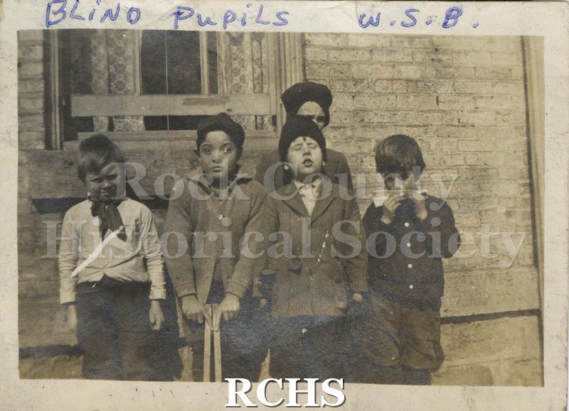 Black and white photograph of the Wisconsin School for the Blind. Shows five unidentified children in front of a building.
