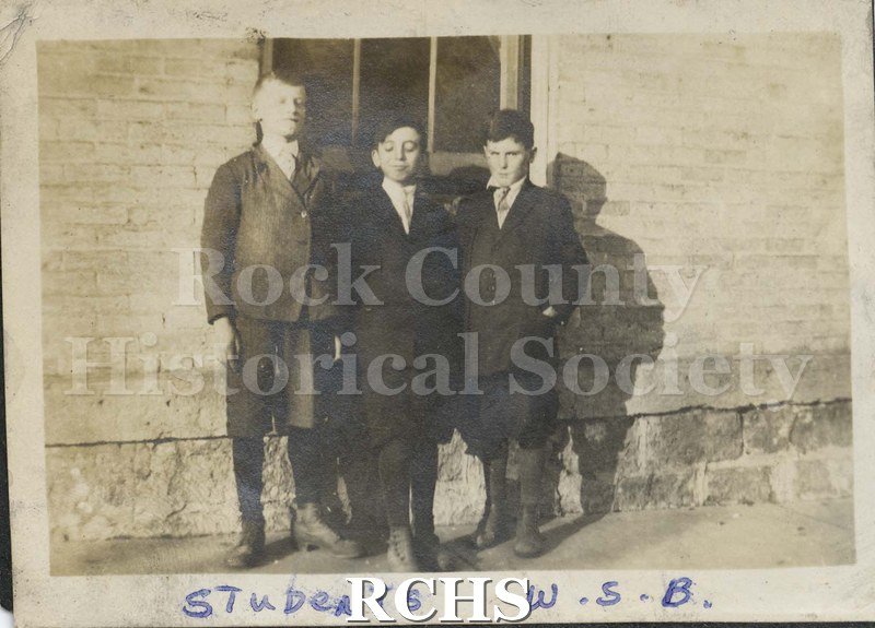 Black and white photograph of the Wisconsin School for the Blind. Shows three unidentified boys standing in front of a building.
