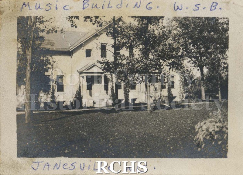 Black and white photograph of the Music Building, Wisconsin School for the Blind. Shows a two story building with a porch and trees in front of the building.