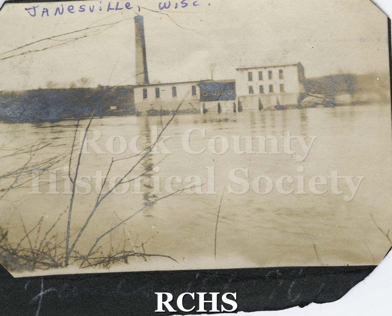 Black and white photograph of Wisconsin Power and LIght Power Plant with river in front.