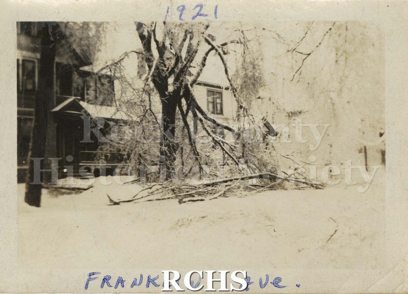 Black and white photograph of an Iice storm in Janesville, Wis. 1921. "Franklin Ave." Shows tree with fallen branches from the ice in front of a two story white.