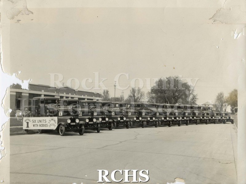 Black and white photograph of E. H. Swegman standing in front of a line of Chevrolets, each with a number visible in the window.