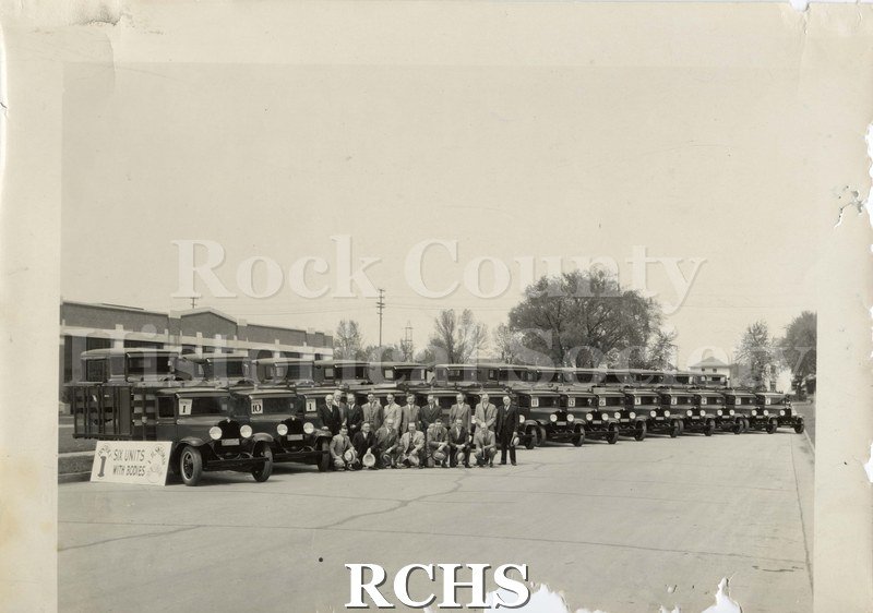 Black and white photograph of E. H. Swegman with Chverolet cars. Sixteen men are standing in front of a line of Chevrolets, each with a number visible in the window.