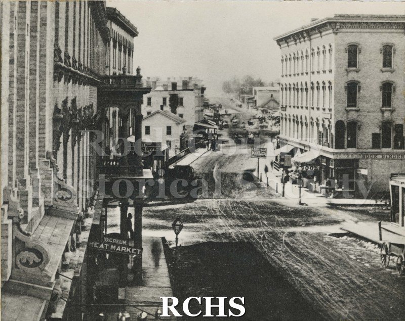Black and white photograph of Milwaukee Street-Early Janesville, WI. Shows four story building on right with words "Books Book Binder" .