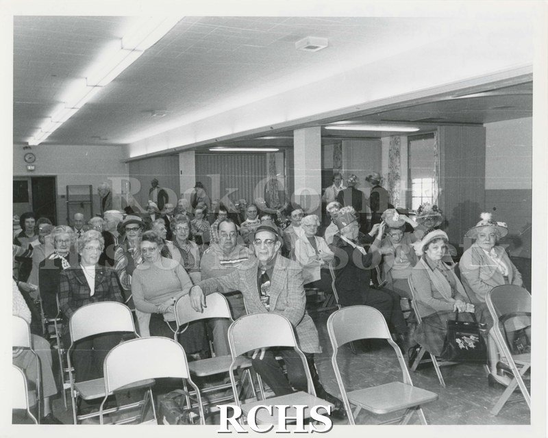 Black and white photograph of the AARP Meeting April 10, 1980. Shows a group of men and women sitting in chairs at a meeting.