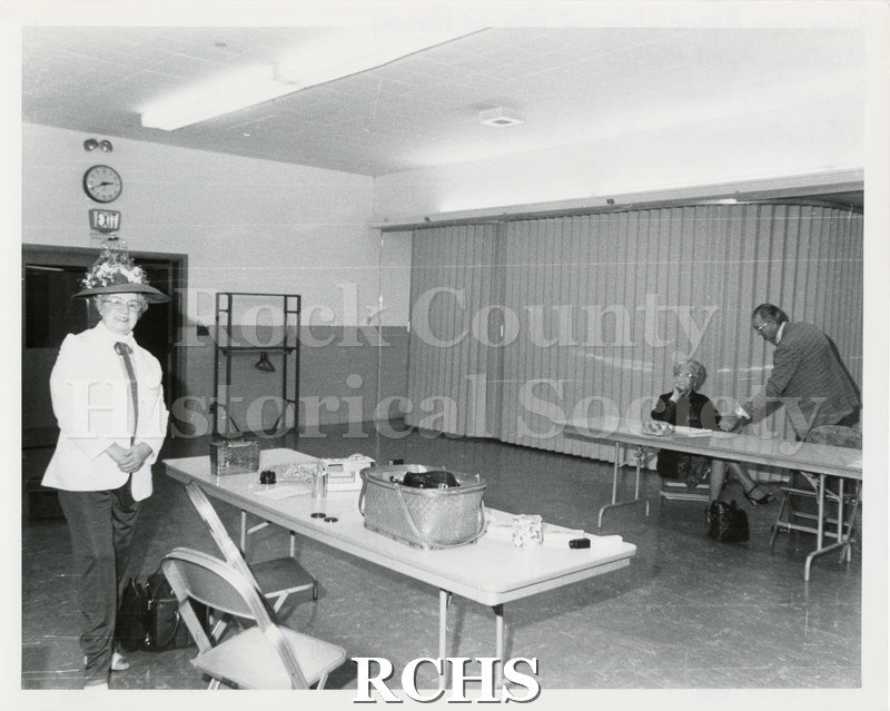 Black and white photograph of Lucille Gotsick standing beside a folding table. There is a basket and other items on the table.