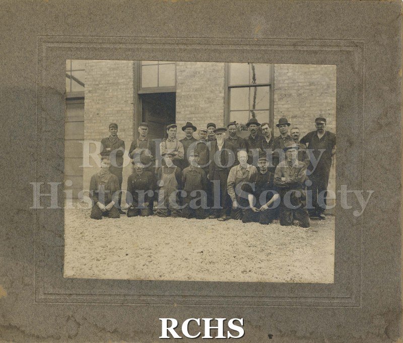 Black and white photograph of twenty men standing and kneeling in front of the roundhouse.