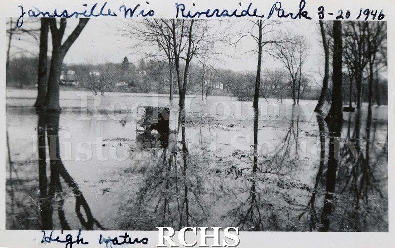 Black and white photograph of Riverside Park. Shows trees in water in foreground with houses in the background. Trees are reflected in the water.