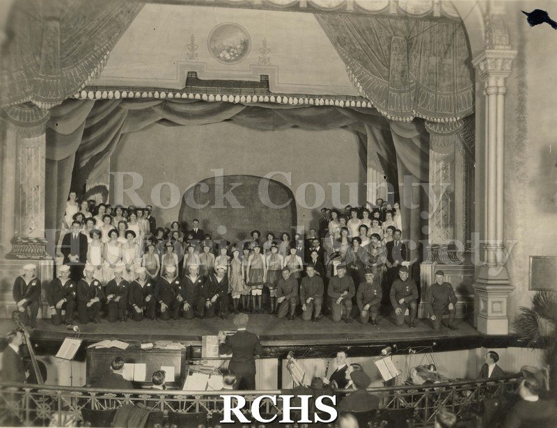 Black and white photograph of the Follies of 1923. Shows several people on stage with the orchestra in the pit below.