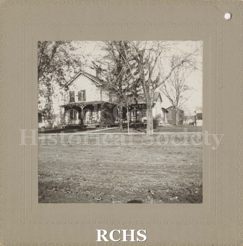 Black and white photograph of the Hiram Spencer Home, Evansville, WI. Shows a two story house with a one story addition on the right and a barn in the background.