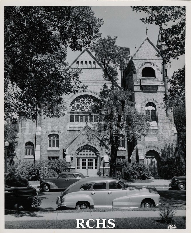 Black and white photograph of the First Baptist Church with cars parked in front.