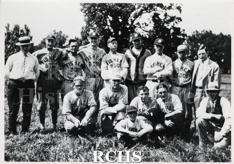Black and white photograph of the Fisher Body baseball team. Shows ten men in uniform and four men in suits. The batboy is sitting in front.