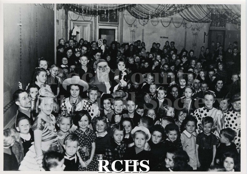 Black and white photograph of the UAW Christmas party for children. Shows Santa Claus in the center holding a child.