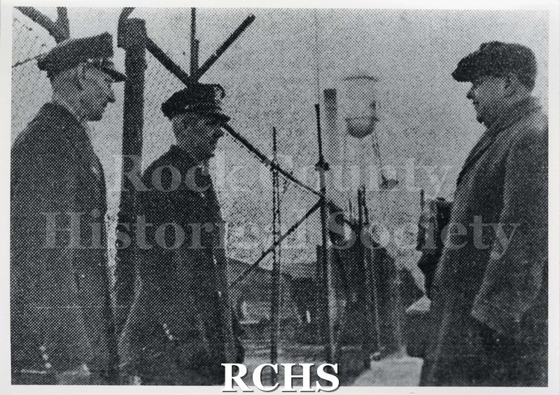 Black and white photograph of the Chevrolet Plant 1937. Shows a newspaper picture of three men standing by a plant fence.