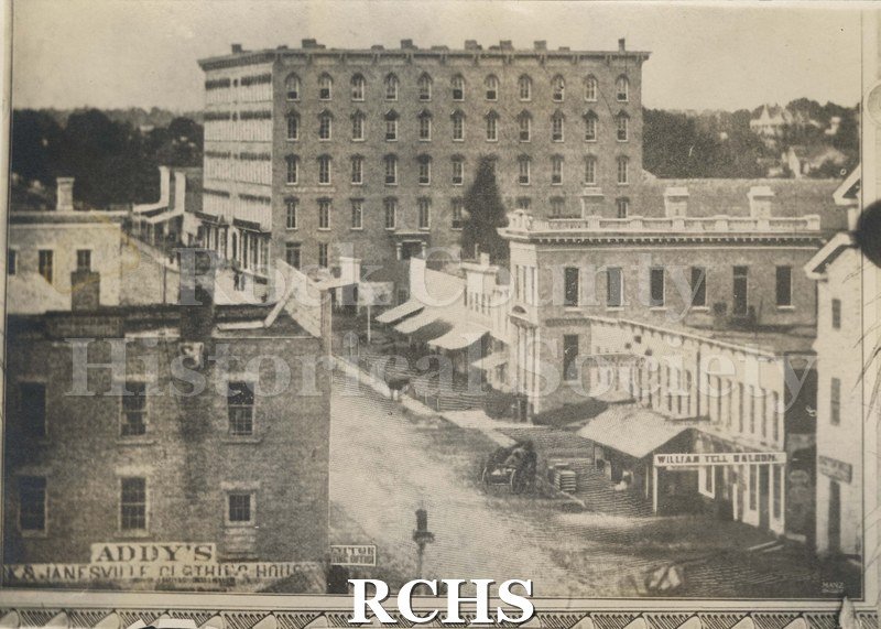 Black and white photograph of early Janesville, showing a street with buildings on each side.