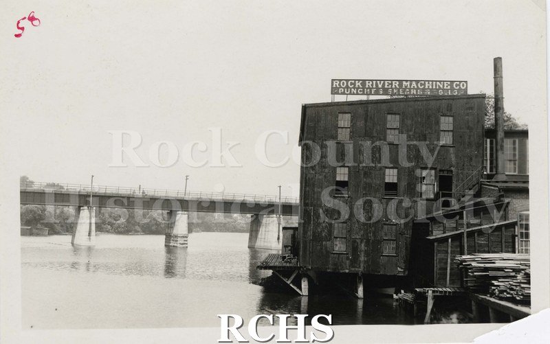 Black and white photograph of early Janesville. Shows the river on the left side with the bridge spanning it.