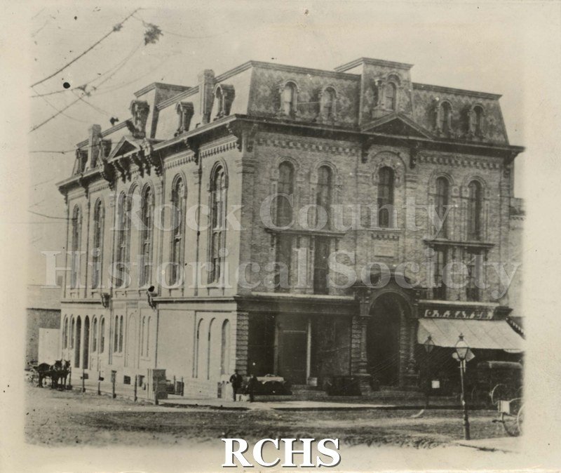 Black and white photograph of Court Street Methodist Church, Janesville WI. There are horses on the street. Church is in a four story building.