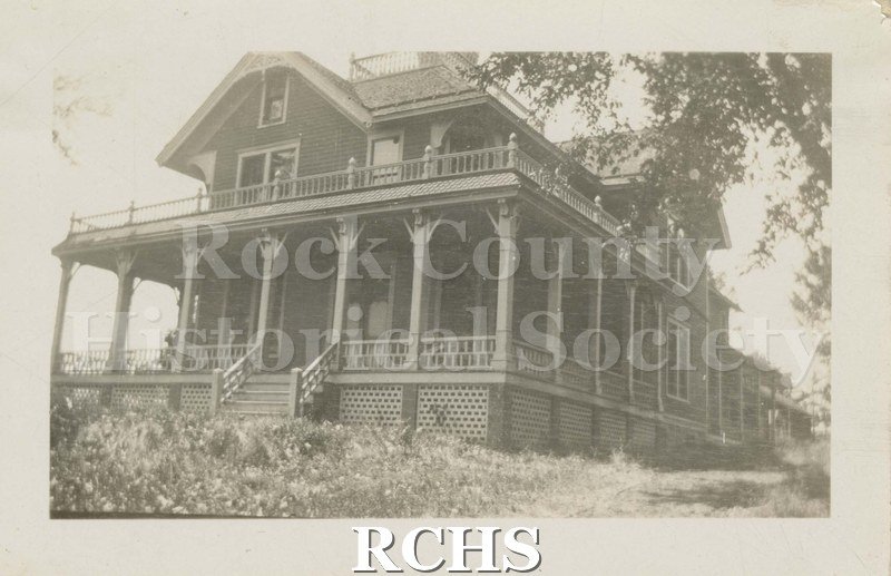 Black and white photograph of the Woodruff Farm House, Janesville, WI. Shows a two-story farm house with a pillared porch and balcony.
