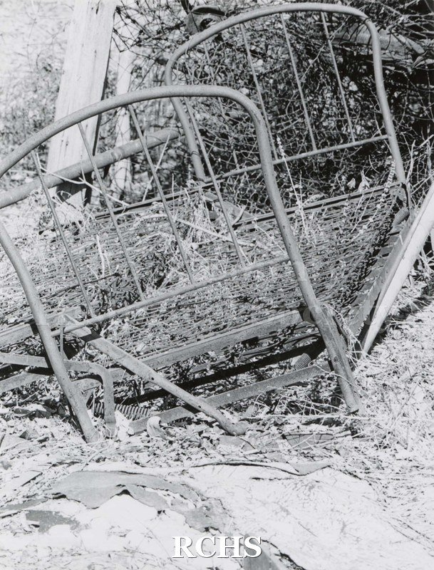 Black and white photograph of Hodson House, Shopiere Road. Shows an abandoned bed disposed of in some brush.