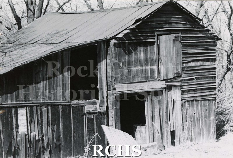 Black and white photograph of Hodson House, Shopiere Road. Shows an abandoned barn. Door is gaping open and boards have been broken off.