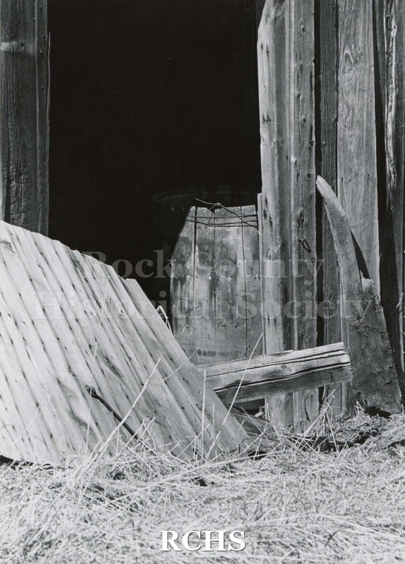Black and white photograph of Hodson House, Shopiere Road. Shows a barn from which the door has fallen off. There is a barrel inside the barn.
