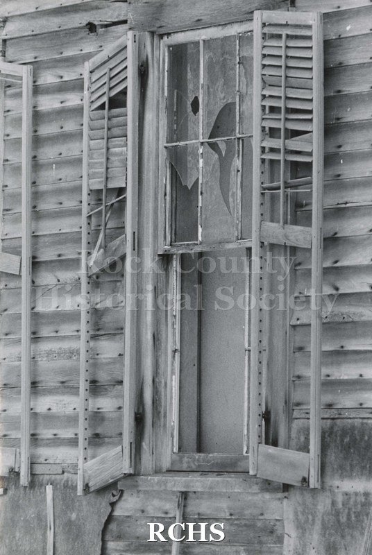 Black and white photograph of Hodson House, Shopiere Road. Shows an abandoned farm house, showing the deterioration of the siding, windows and shutters.