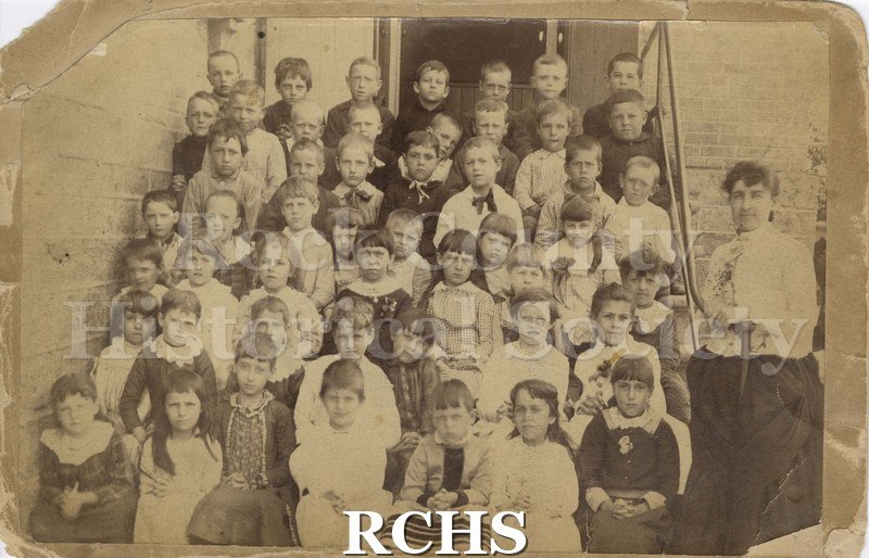 Black and white photograph of 1st Grade Jefferson School, Janesville, WI. School children and teacher are posing on the steps of a school.