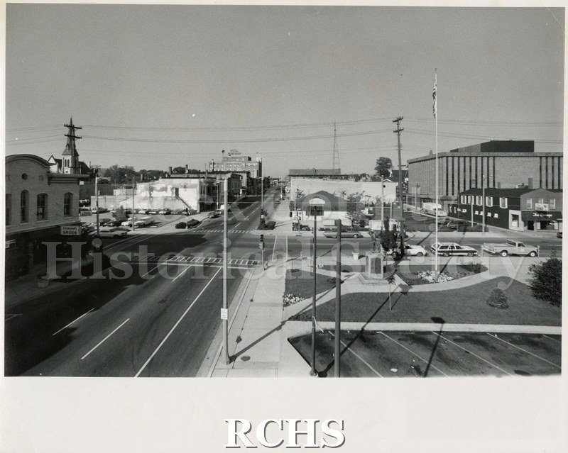 Black and white photograph of Corn Exchange Park and intersection of Frankliln and Milwaukee Streets in Janesville, WI. Hotel Monterey is visible in the distance.