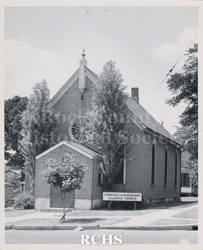 Black and white photograph of Christian and Missionary Alliance Church, Janesville, WI, Shows a brick church with three arched windows on the right side and a.