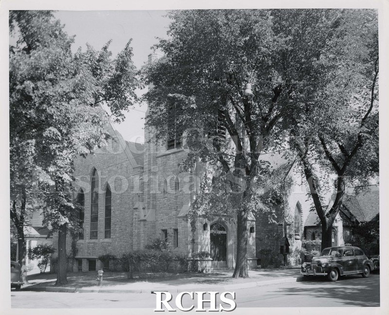 Black and white photograph of Trinity Episcopal Church, Janesville, WI, with several cars parked in front of it.