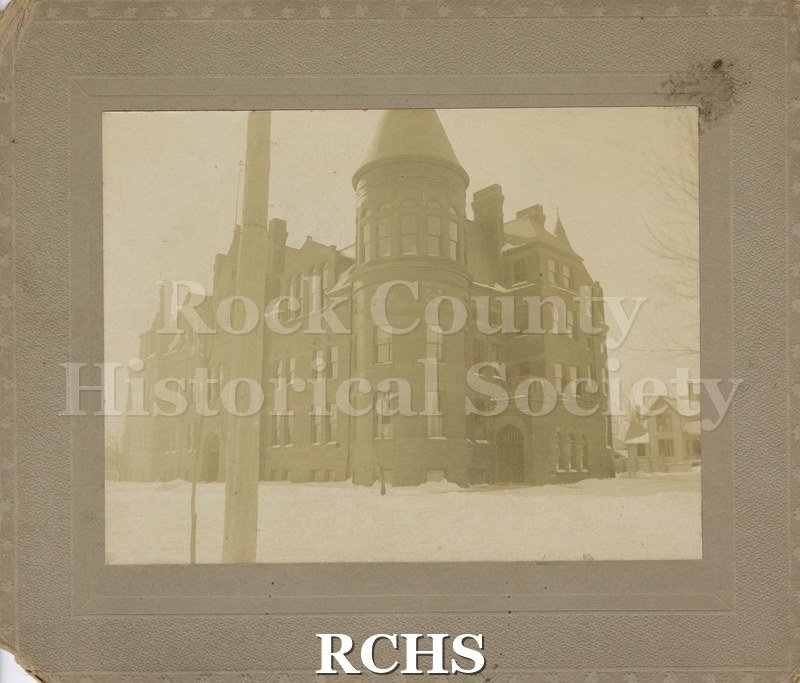 Black and white photograph of Janesville High School from corner. At center is round tower with cone shaped roof.