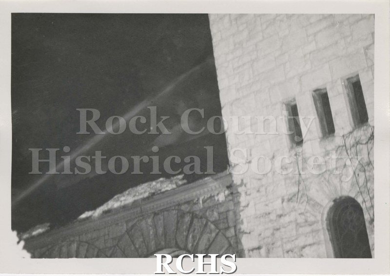 Black and white photograph of the fire at Beloit College Eaton Chapel. Shows part of stone building with arches on lower section and small windows on taller section.
