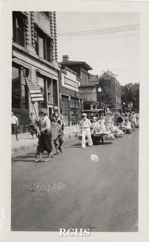 Black and white photograph of Children's Parade, Memorial Day 1933. Shows children marching in a line in front of stores on street.