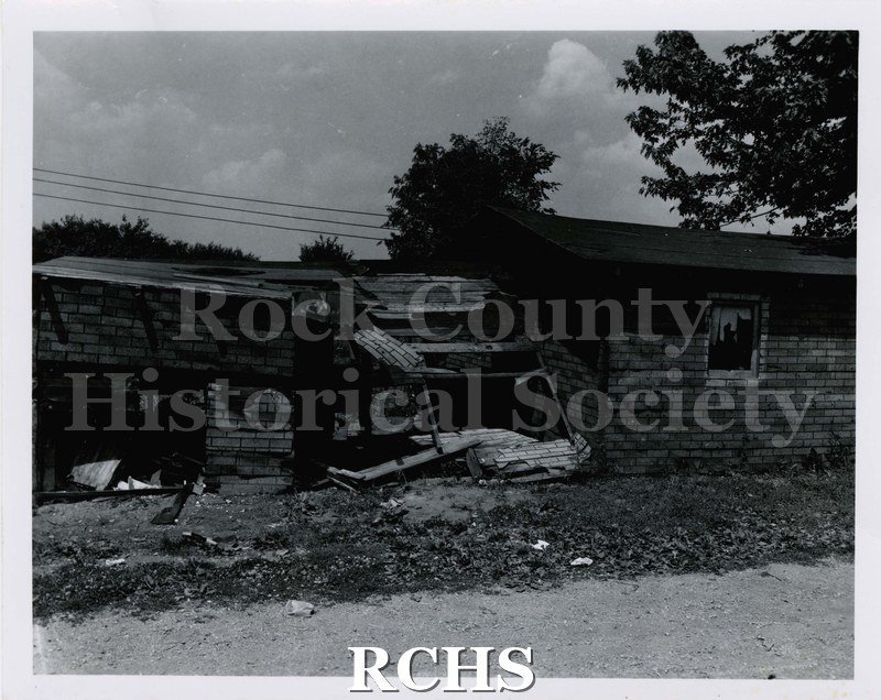 Black and white photograph of 1924 S. Grant St., Janesville, WI. Shows a building that is falling down. Debris is visible in front of the structure.
