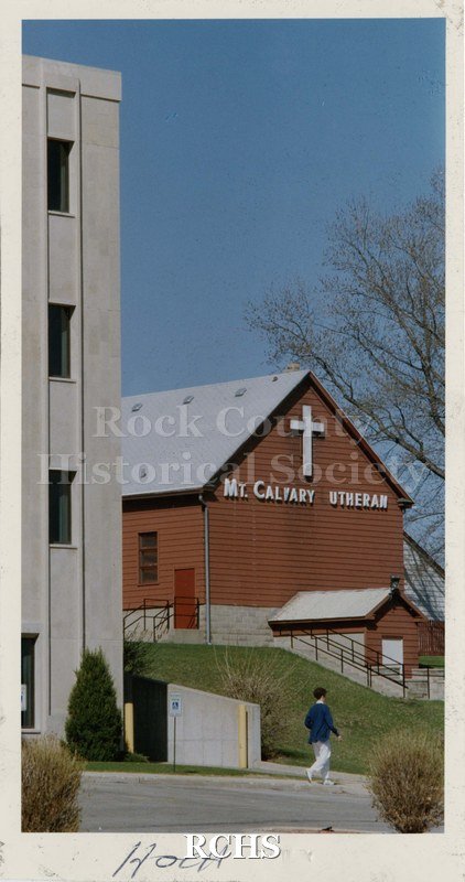 Colored photograph of Mt. Calvary Lutheran Church from the rear. There is a person walking on the sidewalk in front of the building.