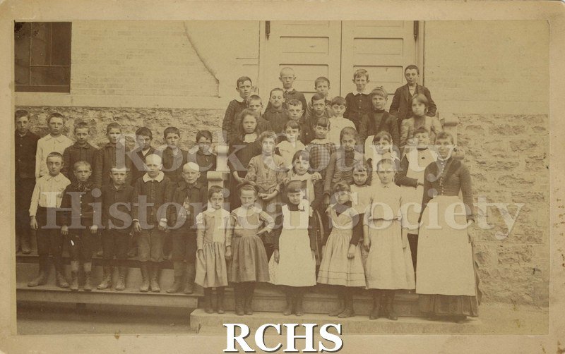 Sepia photo of Adams School 3rd reader scholars and teacher posed in front of a school building.