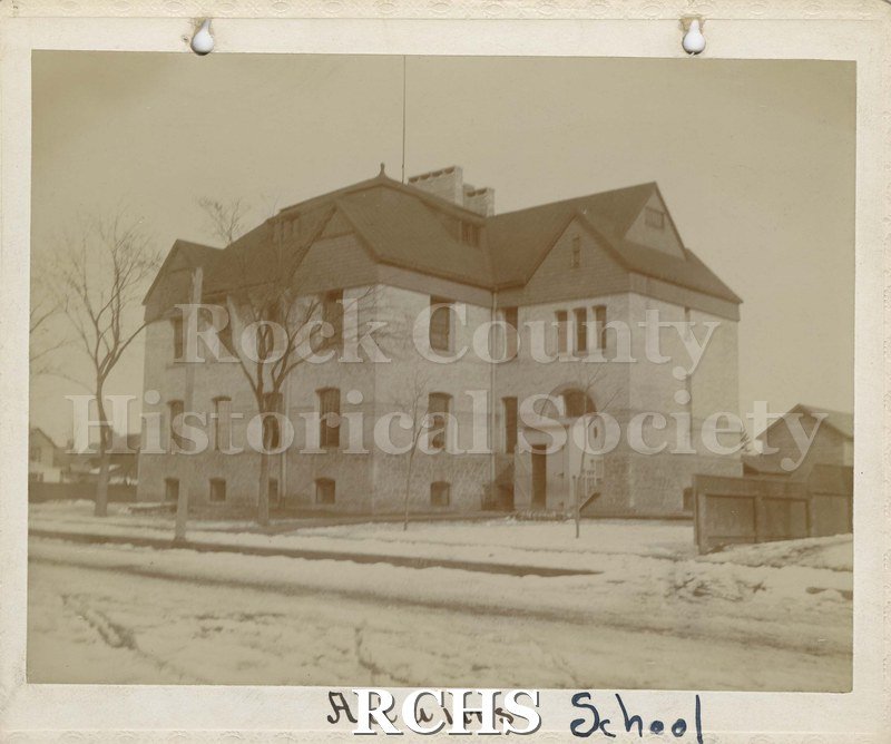 Black and white photograph of Adams School, Janesville, WI, a three story brick building with snow on the ground. On bottom: "Adams School".