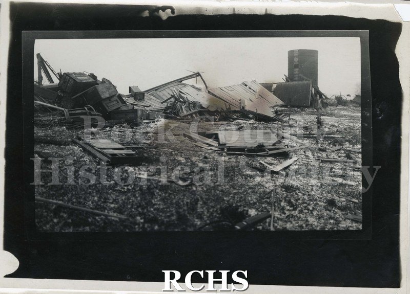 Black and white photograph of tornado of 1911. Shows a building completely demolished by a tornado. Silo is standing without its top.