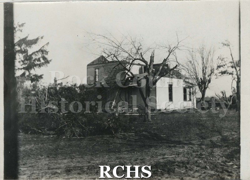 Black and white photograph of a tornado in Rock County 1911. Shows a farm with a farmhouse that has been demolished by a tornado.