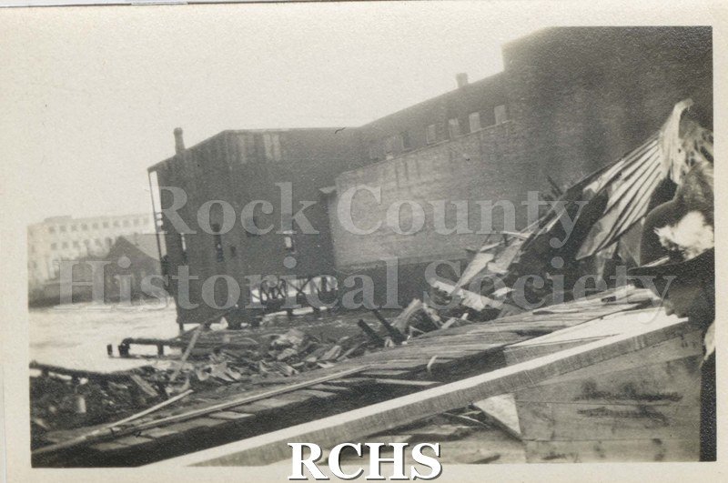 Black and white photograph of Milwaukee Street Fire 1913. Shows damage after a fire. Shows debris in front and scarred building on the right.