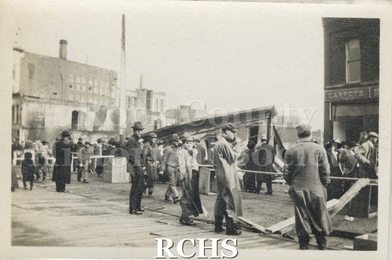 Black and white photograph of Milwaukee Street Fire 1913. Shows people standing on the street, observing the fire damage.