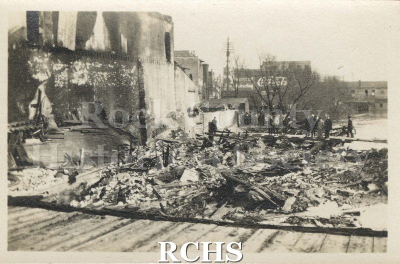 Black and white photograph of Milwaukee Street Fire 1913. Shows damage after a fire. Shows debris in front and scarred building on the left.