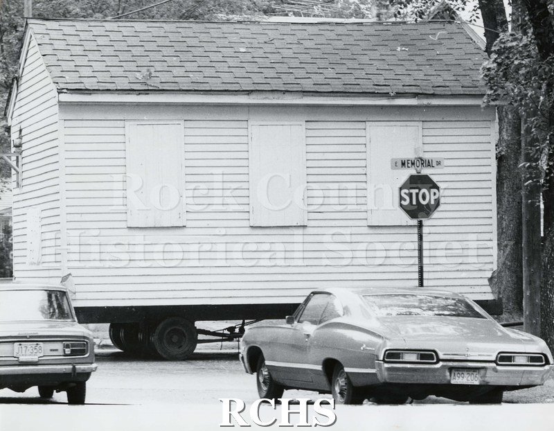 Black and white photograph of the Frances Willard Schoolhouse moving to fairgrounds. Shows progress as it is being moved along the road.