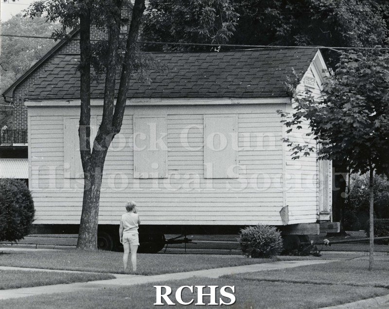 Black and white photograph of the Frances Willard Schoolhouse moving to fairgrounds. It is being moved along the road.