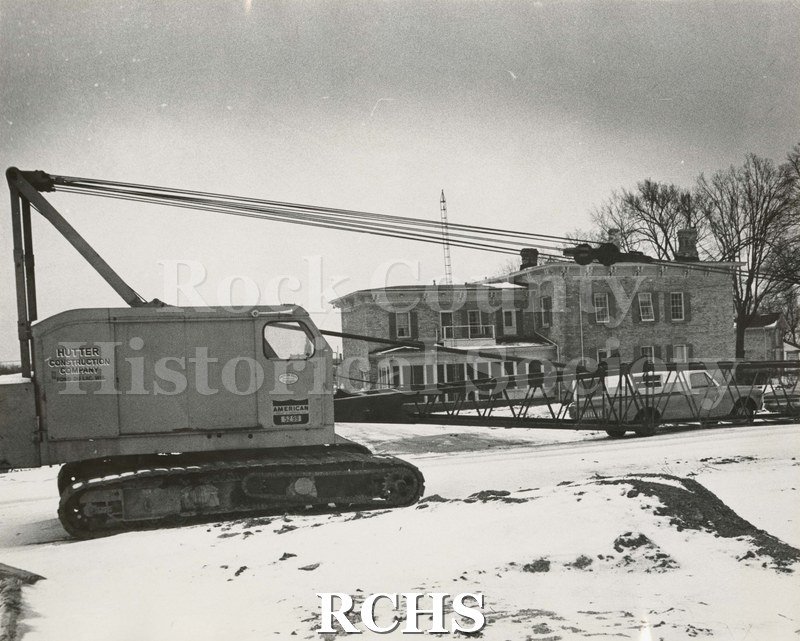 Black and white photograph of Wright-Amato House. Shows a two story house with a crane from Hutter Construction Company, Fond du Lac, Wisconsin, in front of it.