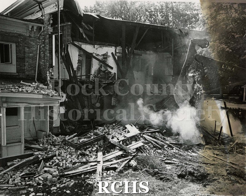 Black and white photograph of the demolition of Wright-Amato House. Crane is on the right with debris in front of the house.