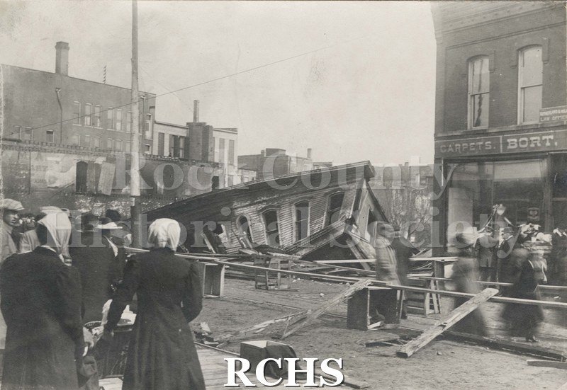 Black and white photograph of the Janesville, WI, fire April 1913. A building that has collapsed is shown in the middle of the picture with debris in front.