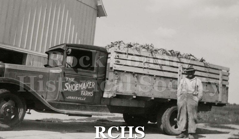 Black and white photograph of a truck with "The Shoemaker Farms Janesville" painted on the driver's door.